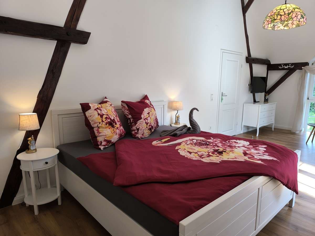 Doppelbett mit bordeauxroter Bettwäsche, Nachttisch und Holzbalkenwerk im Balkonzimmer