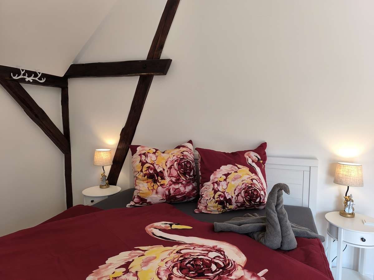 Bett mit bordeauxroter Bettwäsche, floralen Kissen und beleuchteten Nachttischlampen im Balkonzimmer