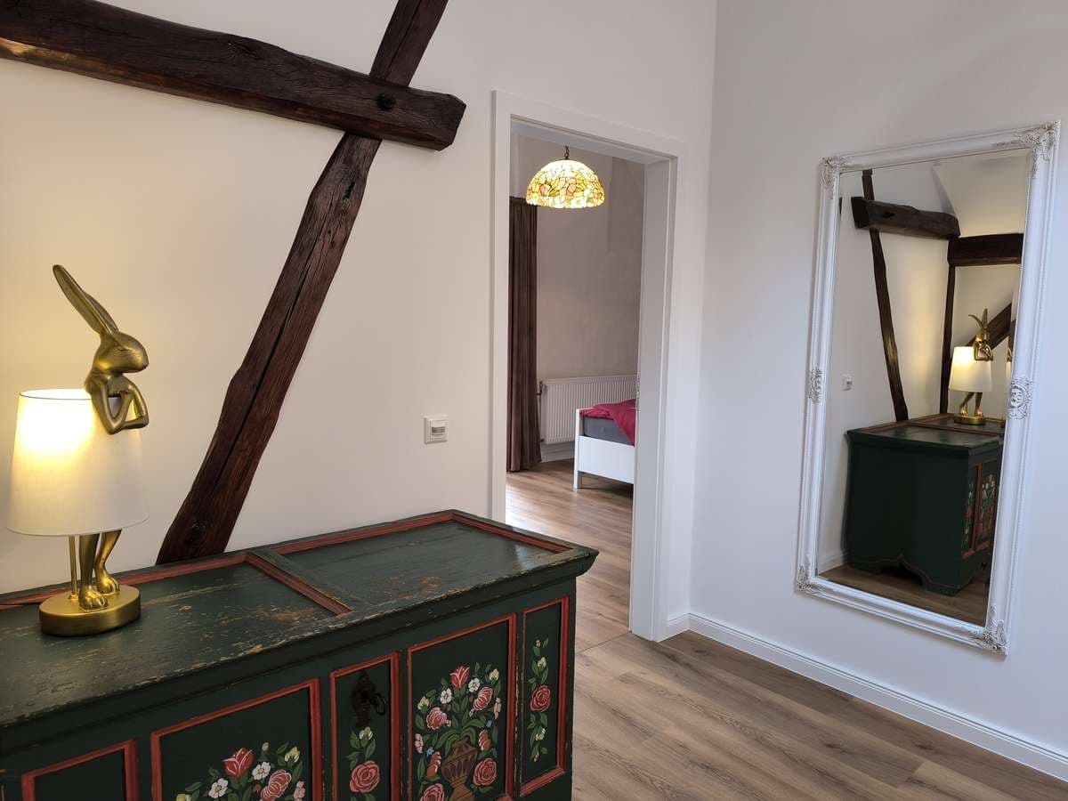Flur im Obergeschoss mit bemaltem Bauernschrank, Spiegel und Blick ins Schlafzimmer