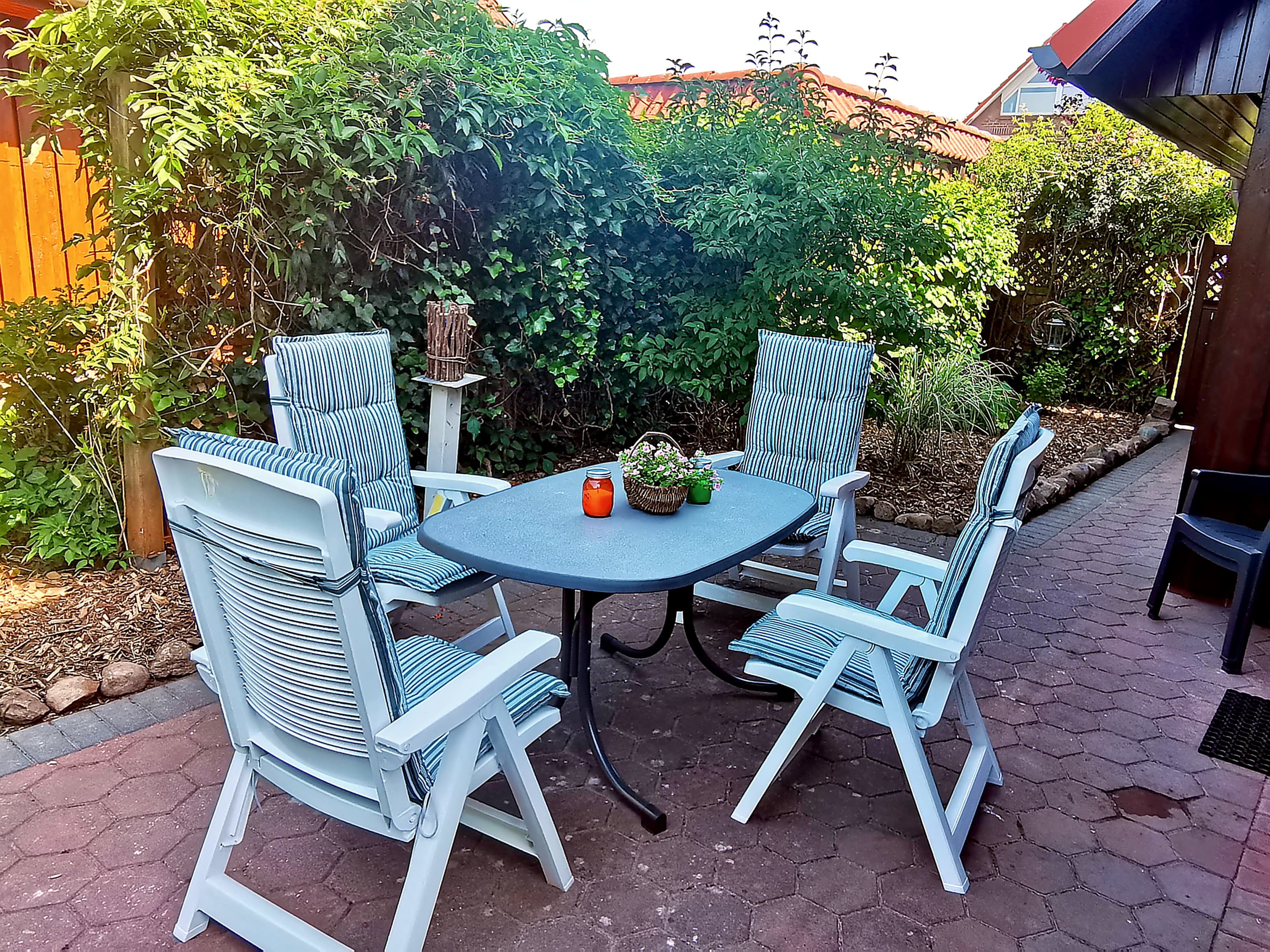 Ein schöner Garten mit einem Tisch und vier Stühlen. Die Umgebung ist grün und einladend.