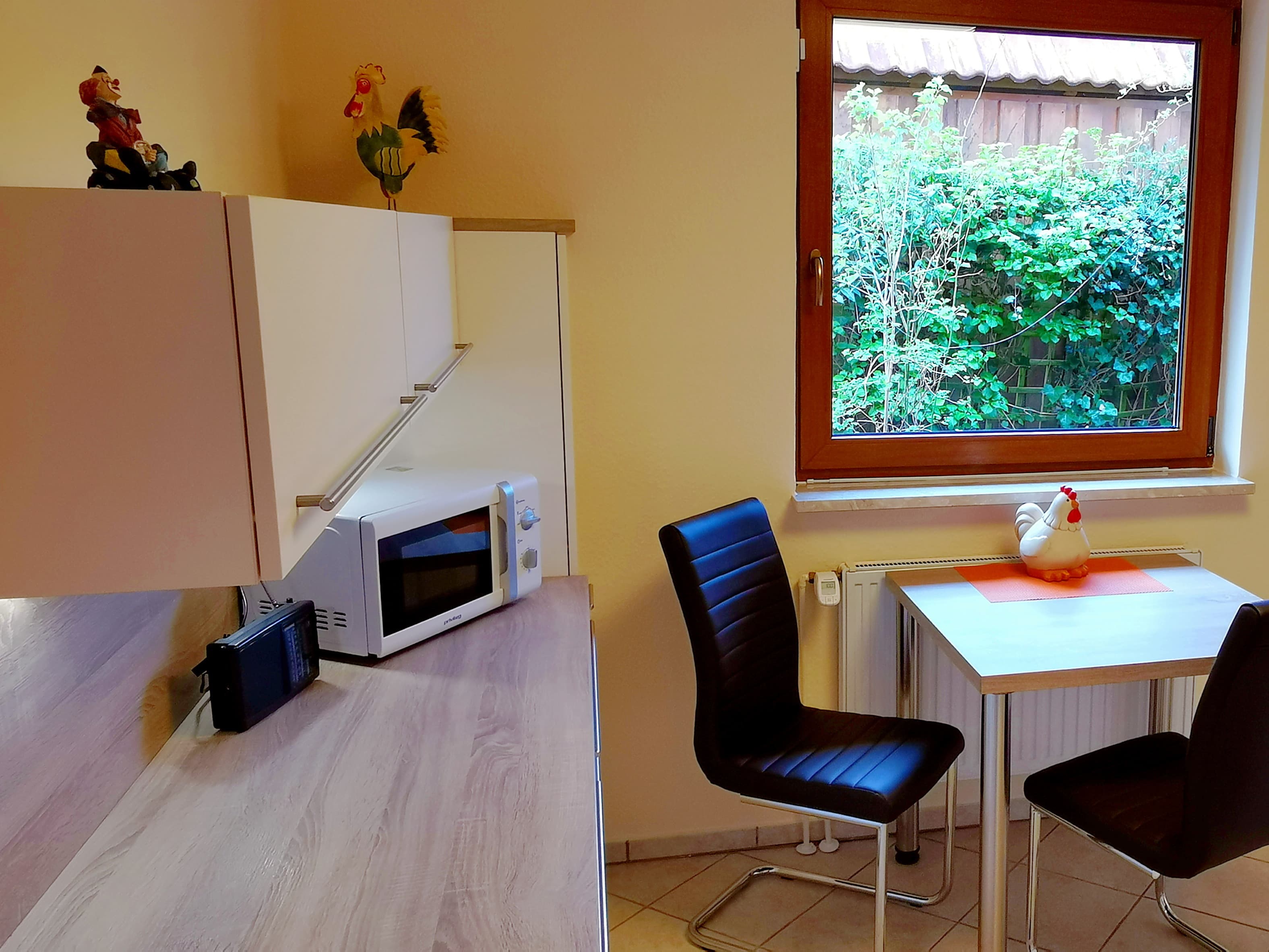 Eine moderne Küche mit einem Tisch und Stühlen. Durch das Fenster sieht man einen grünen Garten.