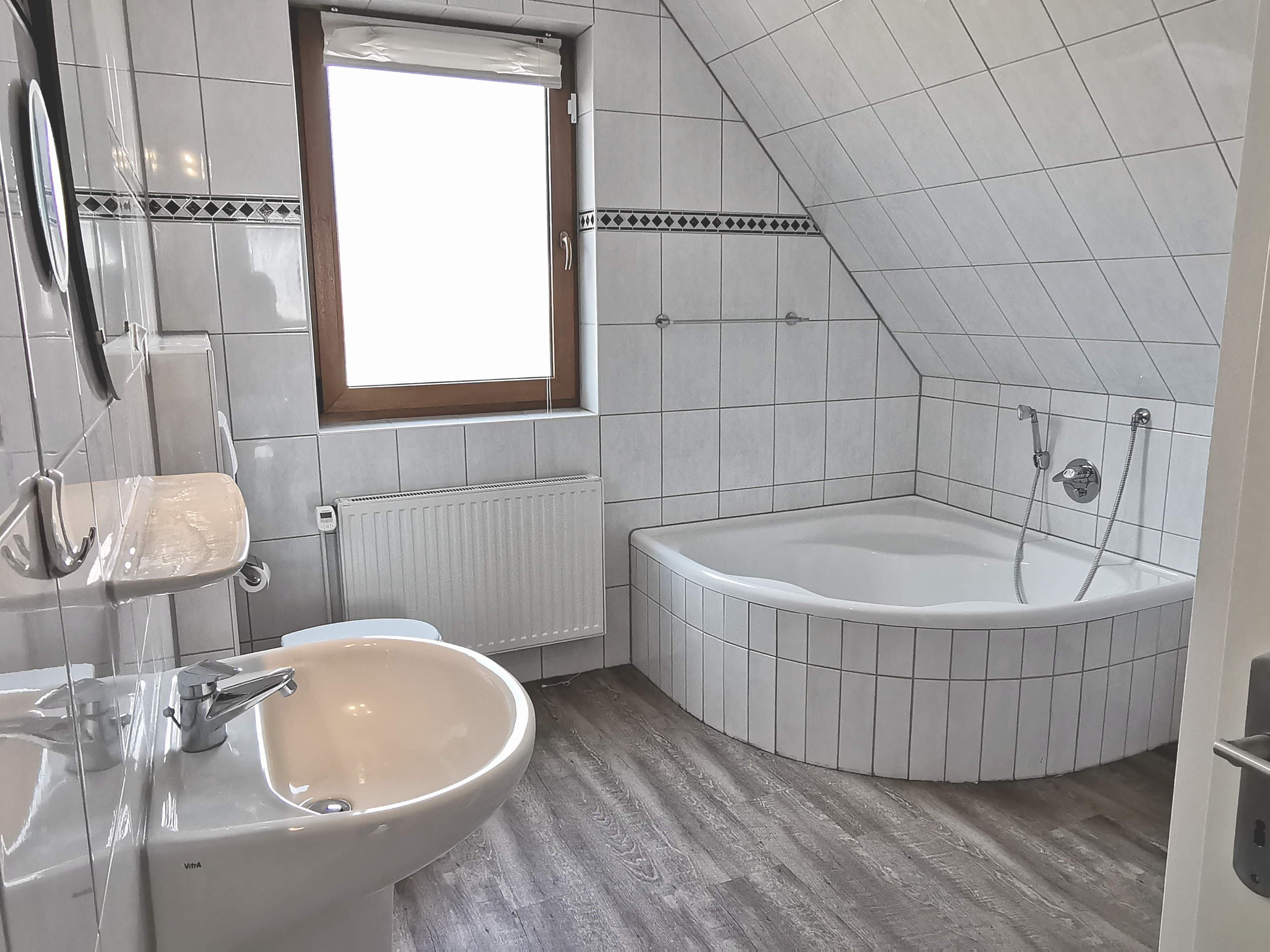 Ein helles Badezimmer mit einer Badewanne, einem Waschbecken und einem Fenster. Die Wände sind mit gefliesten Fliesen in neutralen Farben gestaltet.