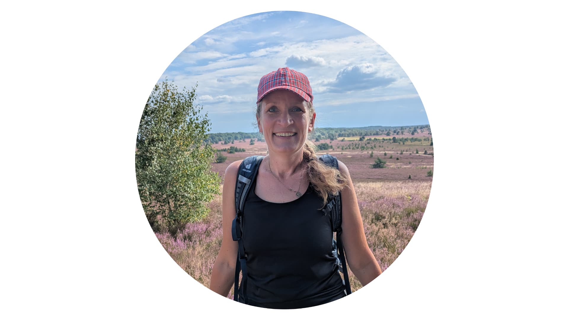Wanderführerin Marthe Kniep mit roter Kappe vor blühender Heidelandschaft.