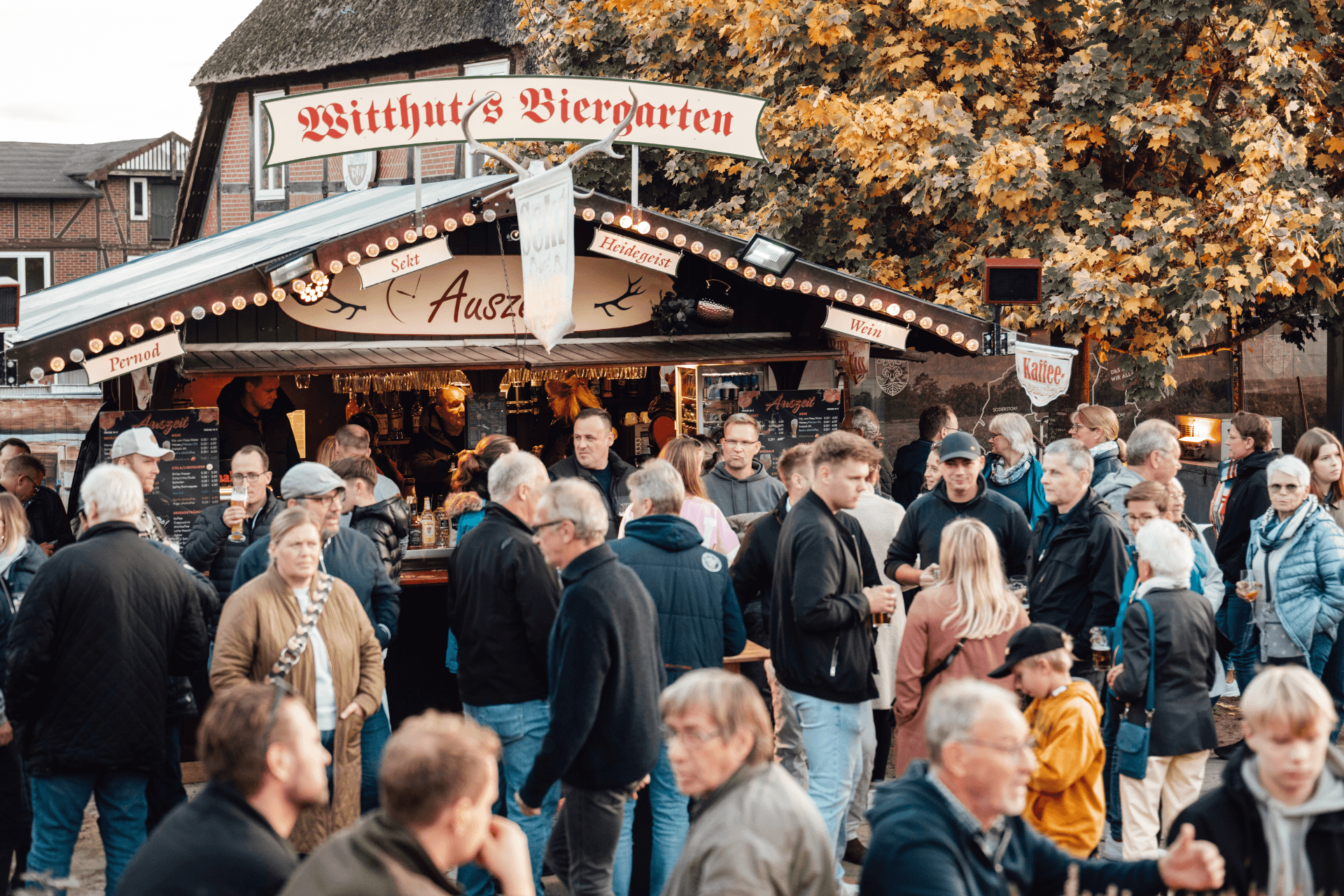 Besucher vor einem Biergartenstand auf dem Herbstmarkt unter buntem Laub.