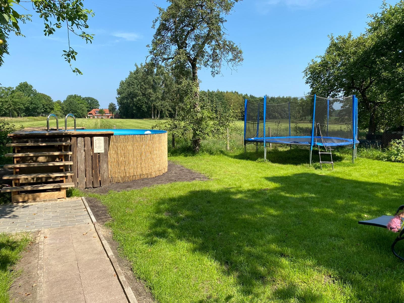Großer Garten mit Aufstellpool, Trampolin, Bäumen und Wiesenblick.