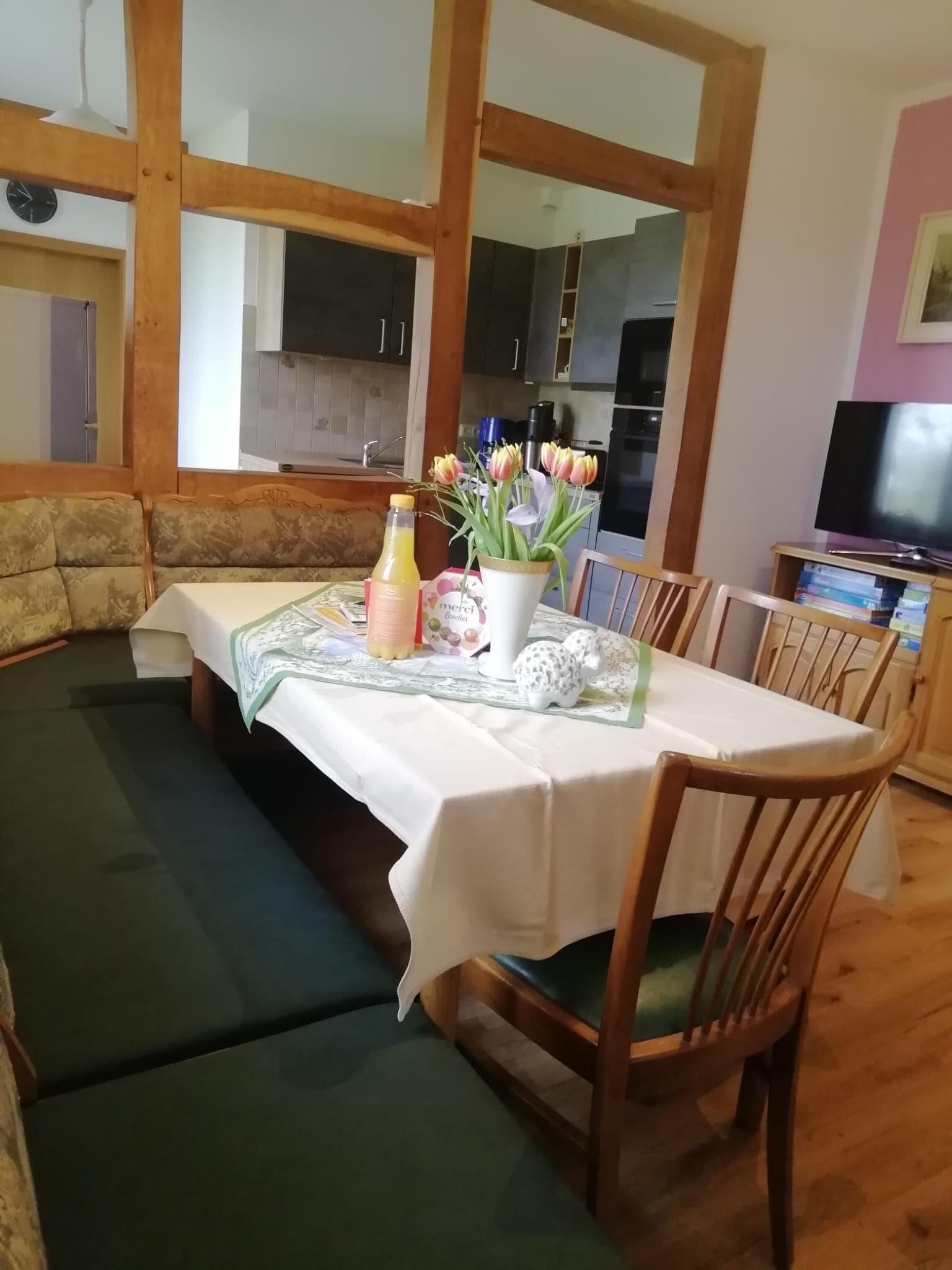 Wohnküche mit Essecke, Holzstühlen, Sitzbank, Blumen auf dem Tisch und Küchenzeile.