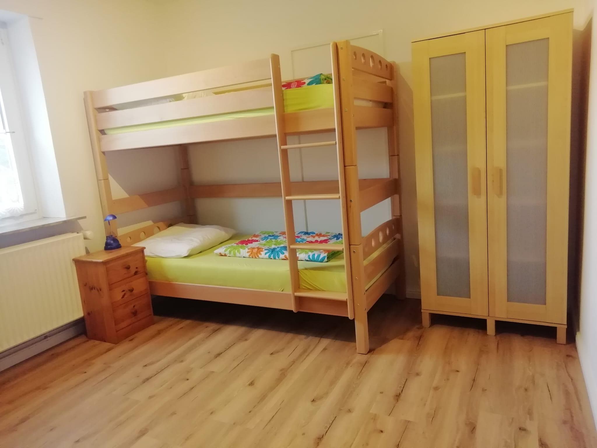 Helles Zimmer mit Doppelstockbett, Kleiderschrank, Nachttisch und Holzfußboden.