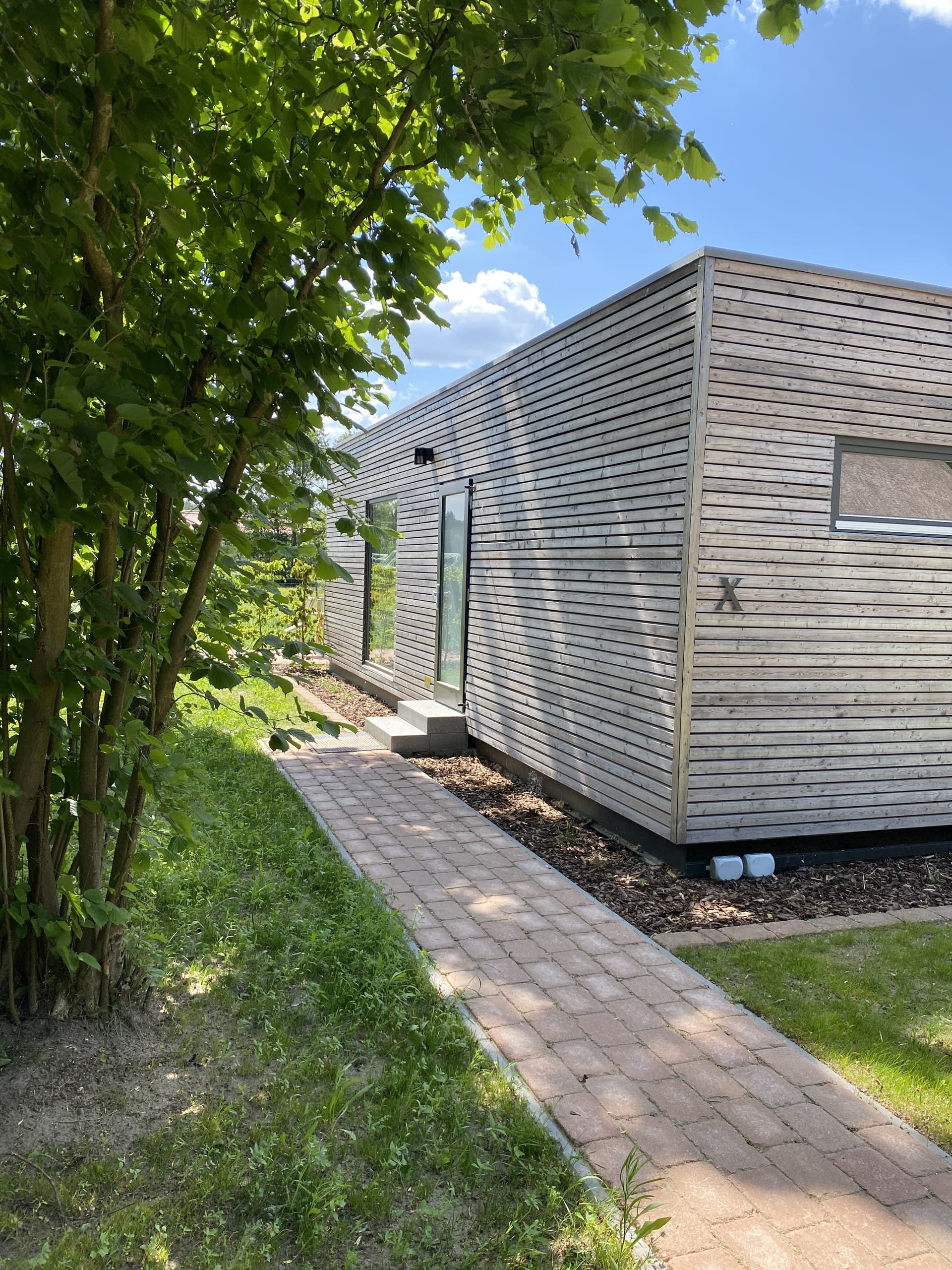 Tiny House X mit Holzfassade und gepflastertem Weg auf dem HofGut Bockelkathen