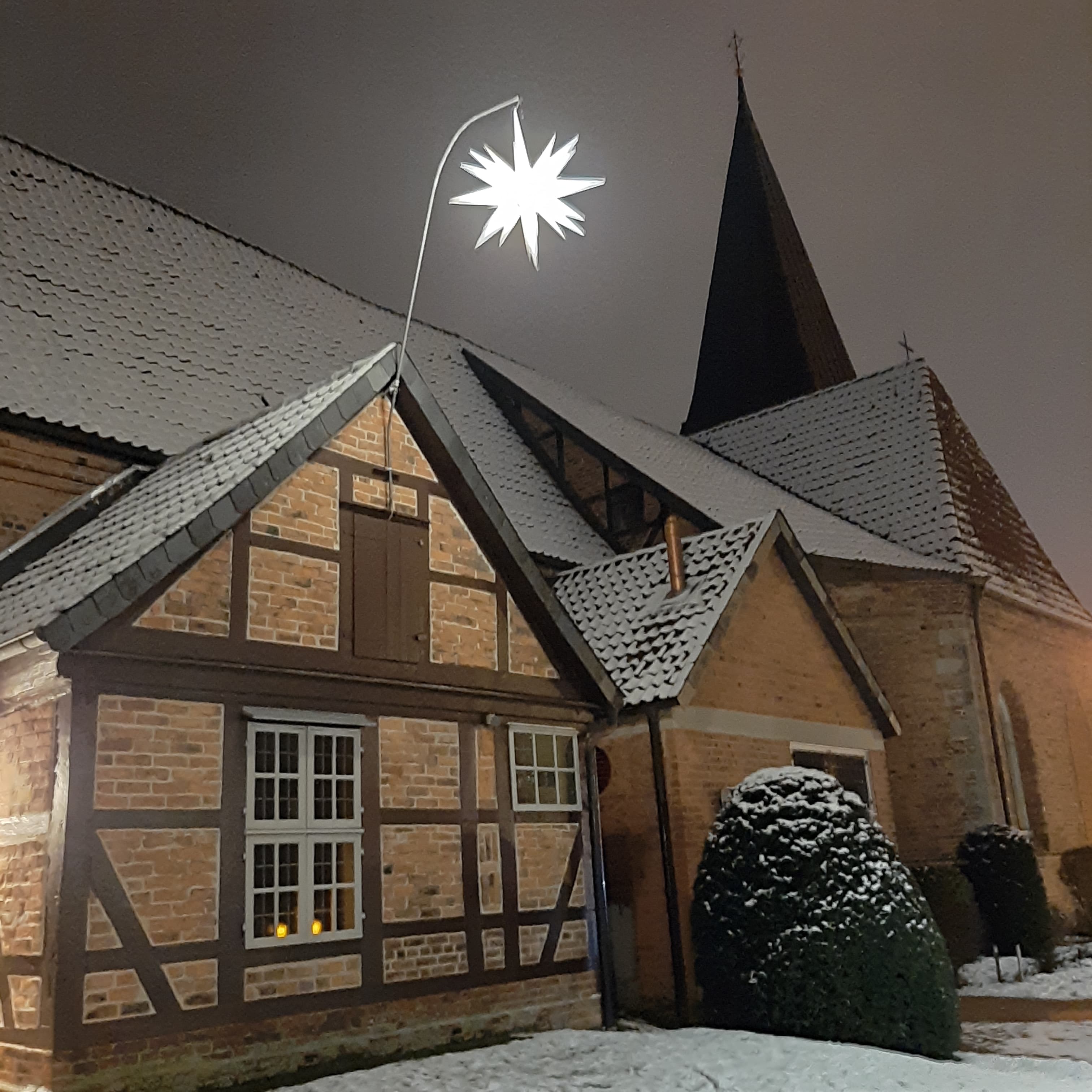 Die Blumläger Kirche im Winter mit schneebedecktem Dach und einem leuchtenden Adventsstern als Dekoration.
