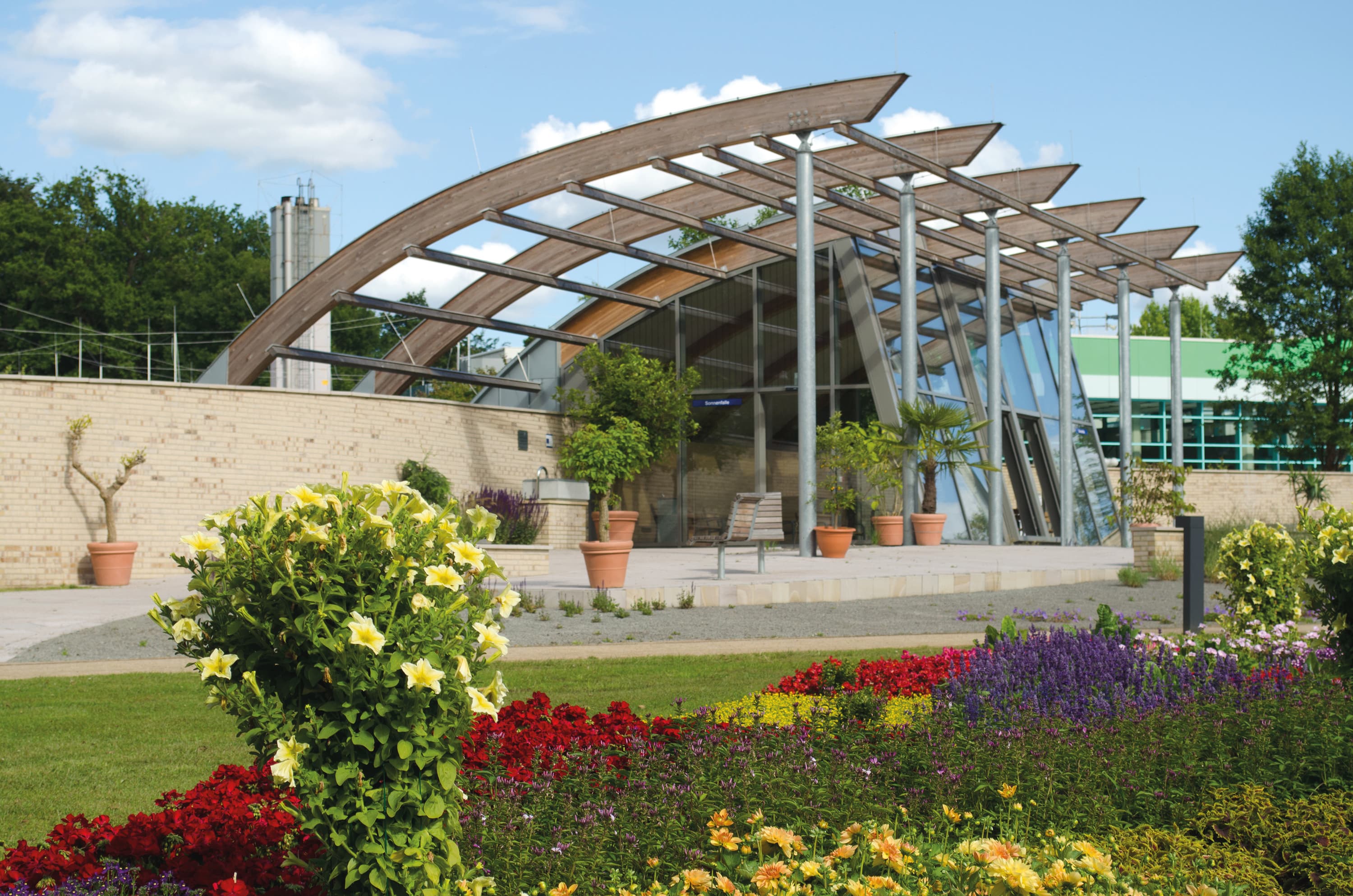 Die Sonnenfalle bietet einen wind- und wettergeschützten Aufenthaltsbereich im Kurpark von Bad Bevensen. Die Glaswand lässt sich über die ganze Front öffnen, vor einer Wärme speichernden Lehmmauer laden hochwertige Holzmöbel zum Sitzen oder Liegen ein.&nbsp;